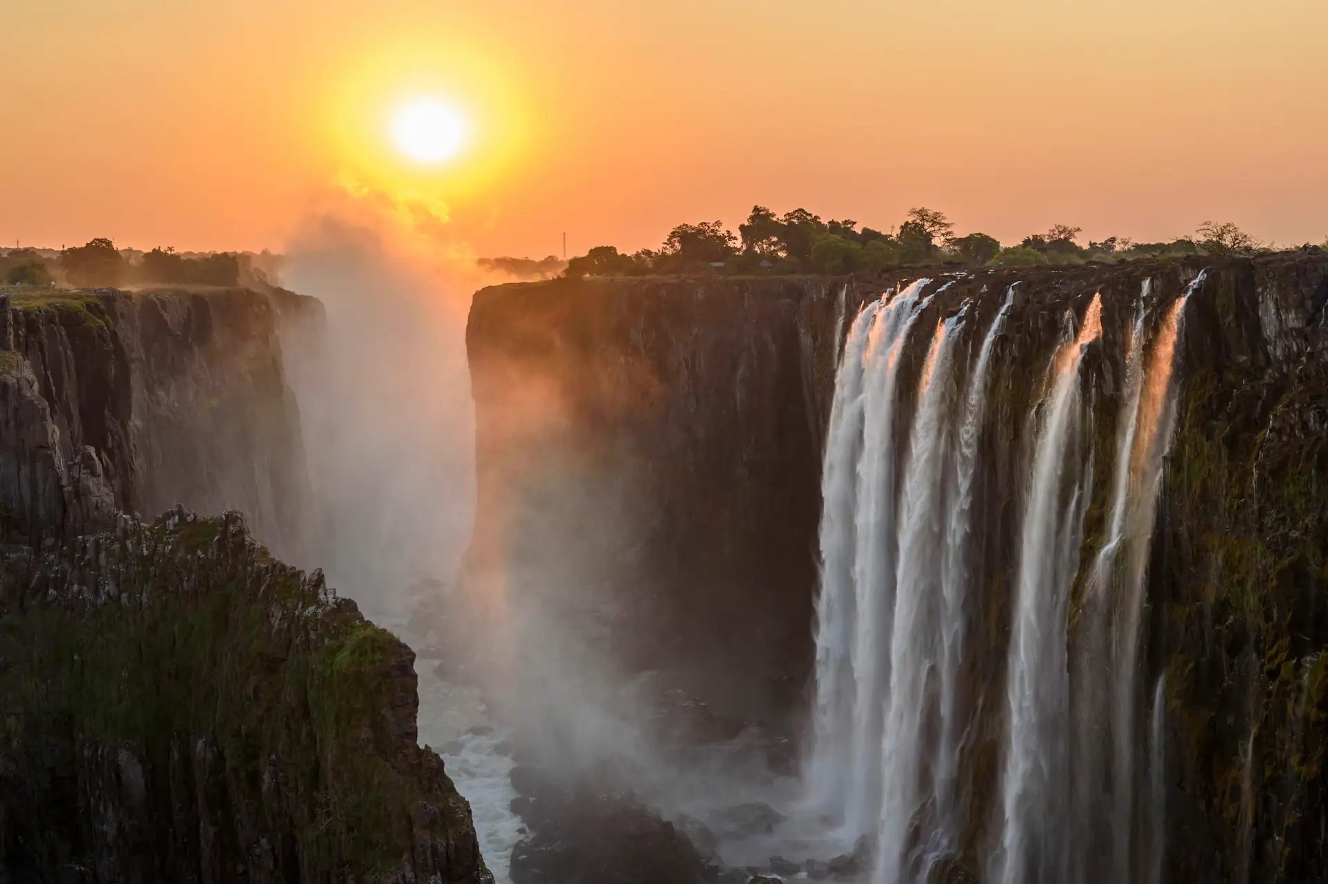 Die Victoria Falls am Sambesi im warmen Abendlicht mit aufsteigender Gischt über der Schlucht