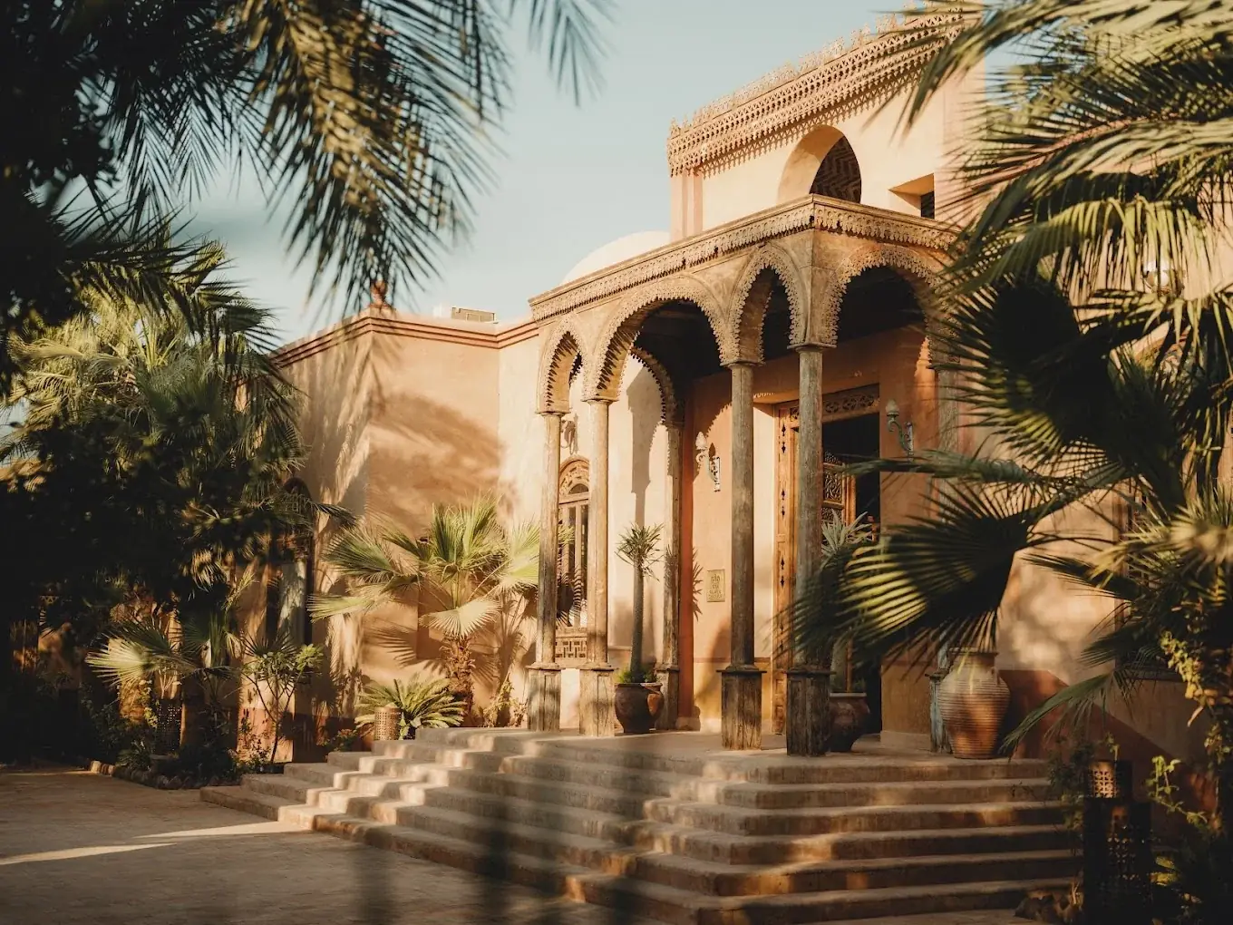Eingang des Al Moudira auf der Westbank von Luxor mit orientalischen Bögen, Säulen und Palmen im warmen Licht