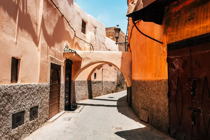 Sonnendurchflutete Gasse in der Medina von Marrakesch in Marokko mit ockerfarbenen Lehmmauern