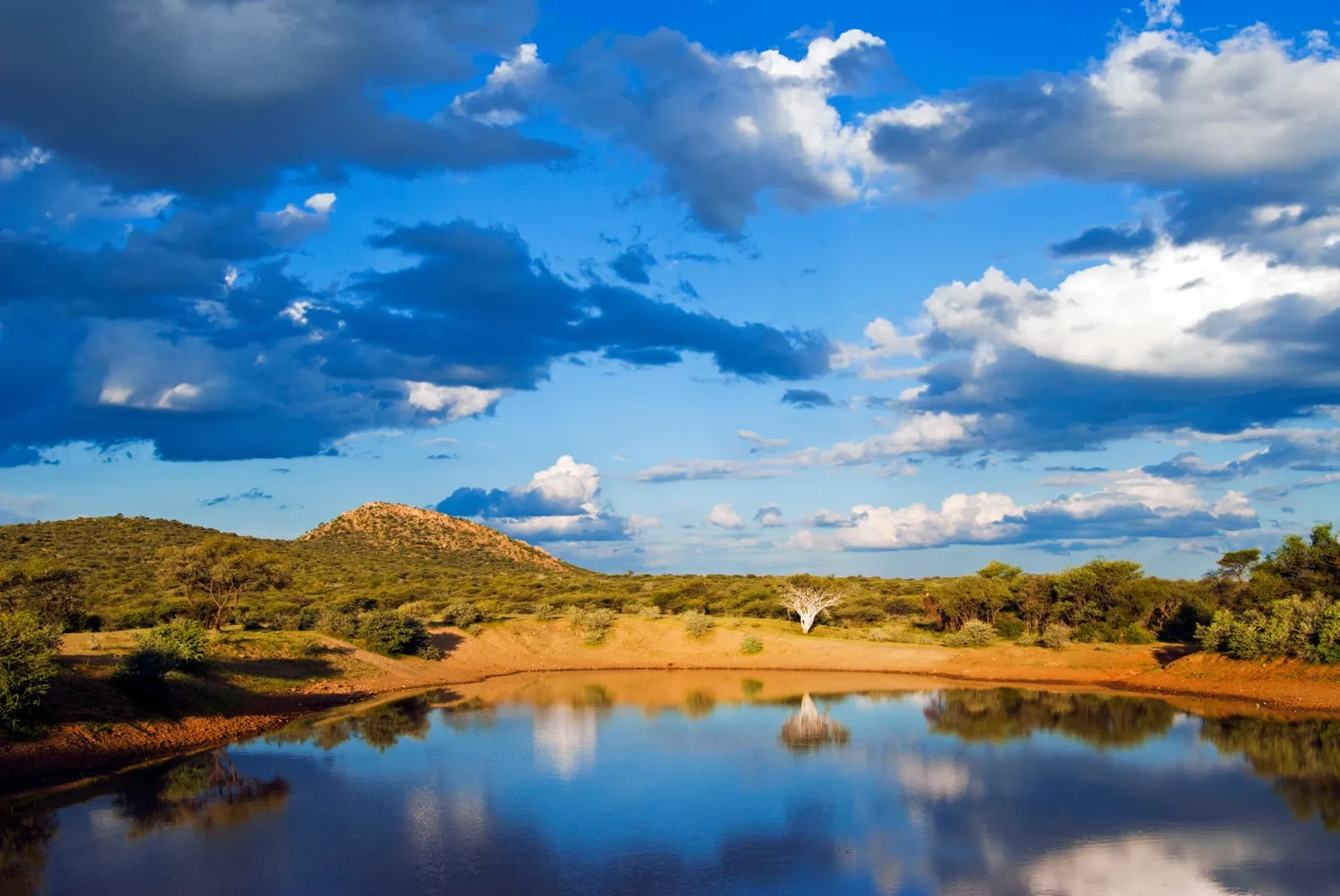 Wasserloch im Ongava-Reservat am Rand des Etosha-Nationalparks unter Wolkenhimmel, Namibia