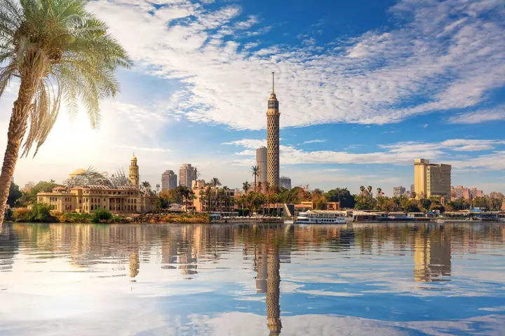 Skyline von Kairo in Ägypten mit Cairo Tower und Palmen am Nilufer, gespiegelt im Wasser